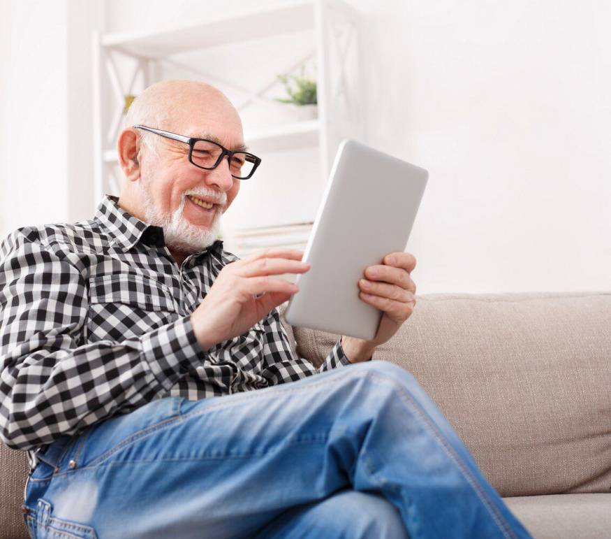 Smiling senior man reading news on digital tablet. Cheerful excited mature male using portable computer at home, copy space